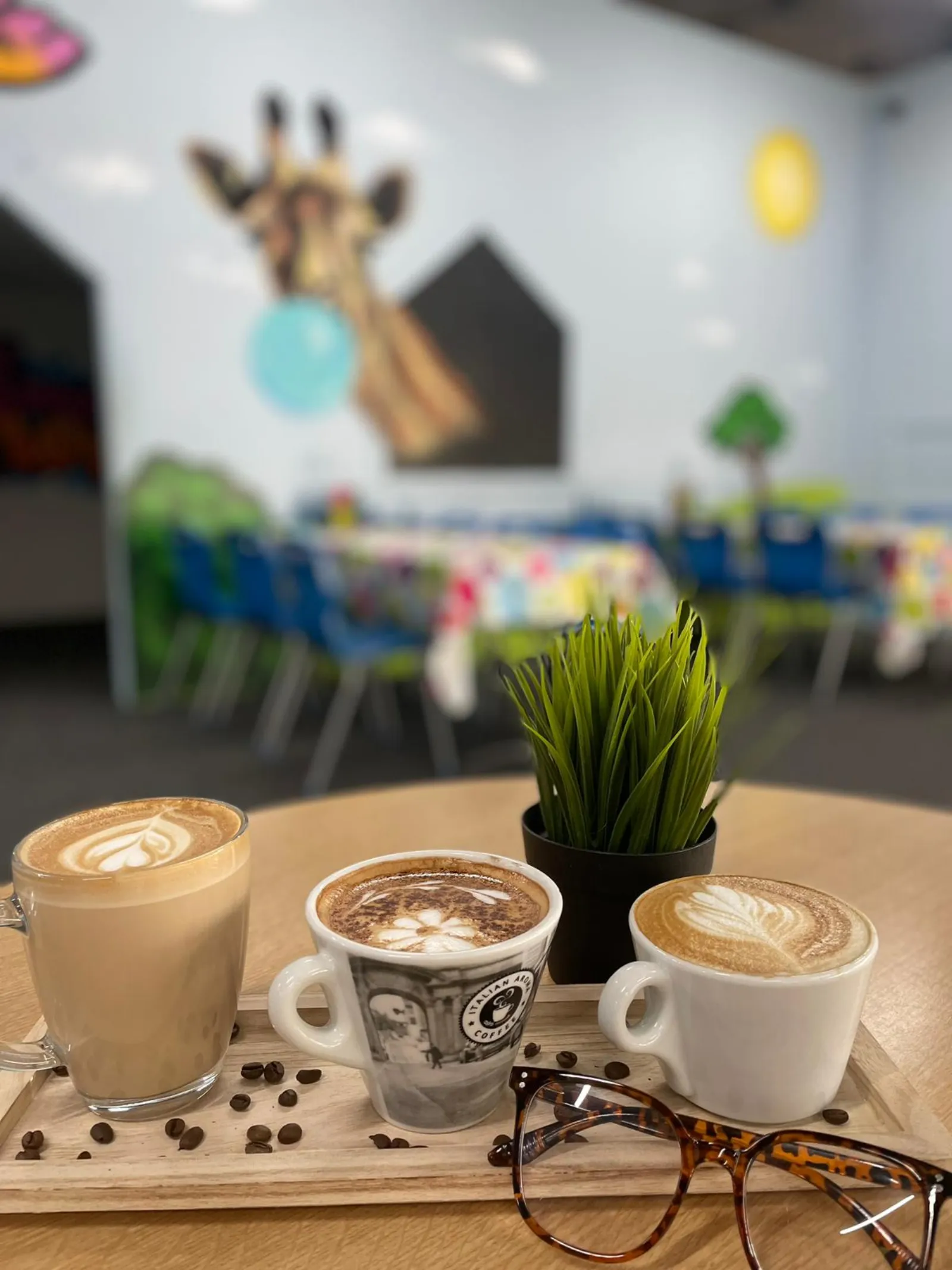 A flight of three coffees on a board in front of the giraffe café mural