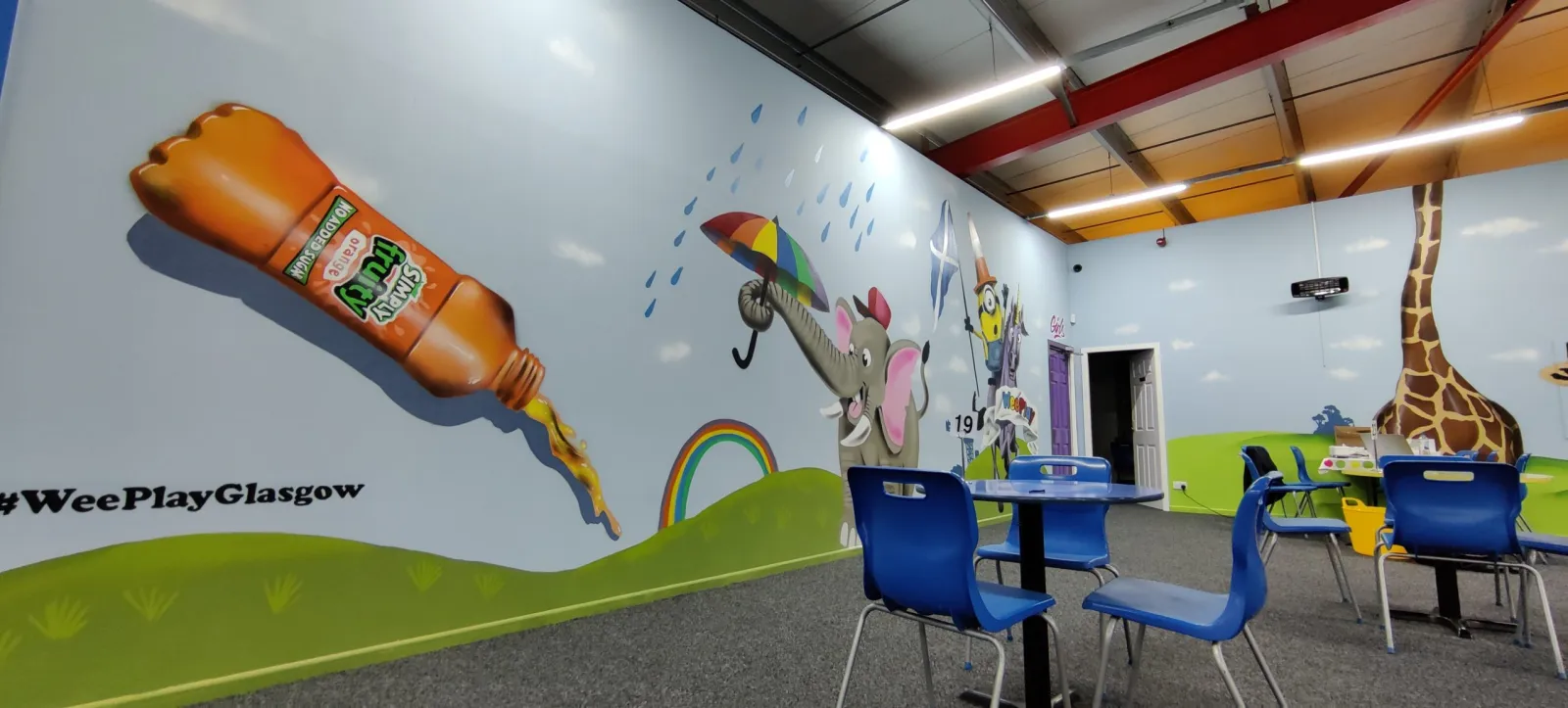 The bright Sip and Sit café seating area at WeePlay, with a colourful wall mural