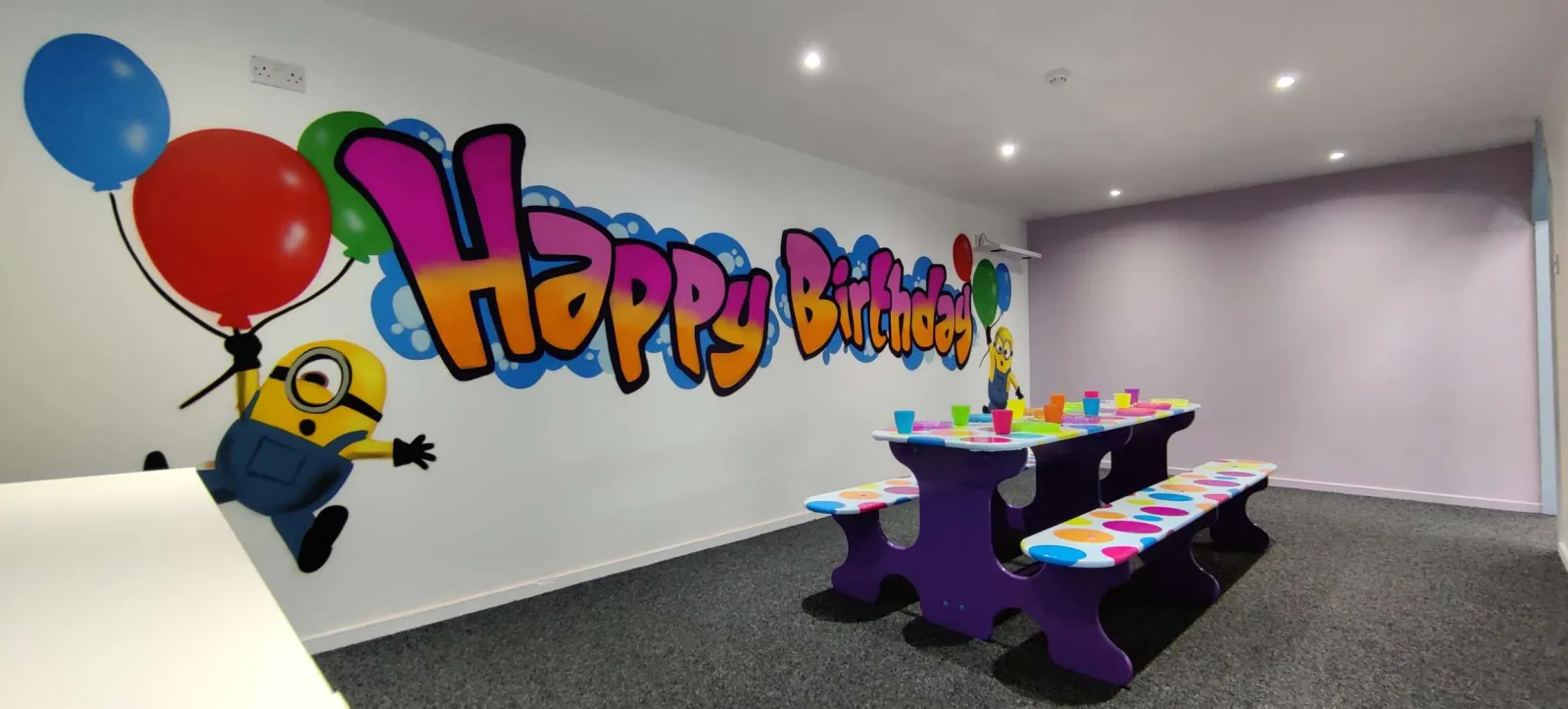 A WeePlay party room with a Happy Birthday mural and a purple party table
